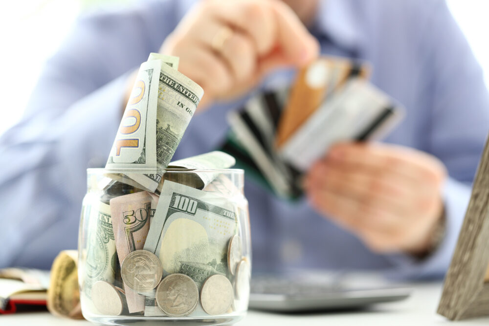 Jar full of money with person organizing credit cards in the background