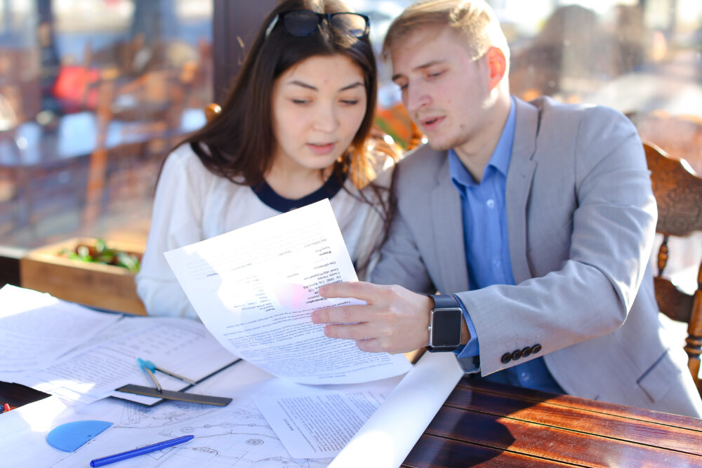 financial planning for young adults - Students calling professor by smartphone to ask about architecture project. Boy and girl drawing with divider and ruler at cafe. Concept of preparing home task and drafting.